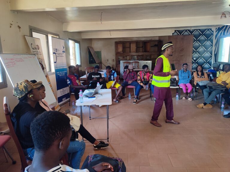 Un animateur en gilet jaune s’adresse à des jeunes assis en cercle lors du lancement de l’École itinérante des VBG