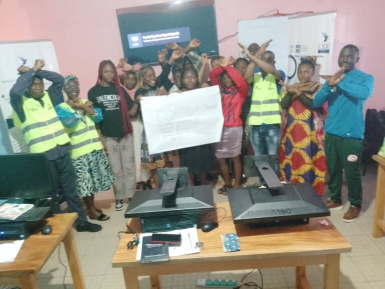 Groupe de jeunes faisant un geste de bras croisés derrière une pancarte lors de l’École itinérante de prévention des VBG